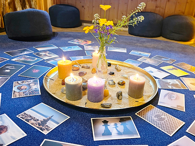 Ein Tablett mit brennenden Kerzen und Blumen ist von Fotos auf einem blauen Teppich umgeben und schafft eine gemütliche und künstlerische Atmosphäre.