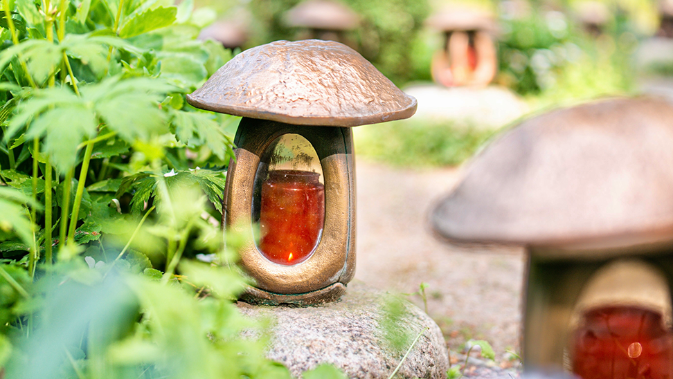 Mushroom-shaped garden lights with amber glass, surrounded by lush green foliage and placed on a stone path.